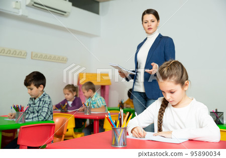 Friendly teacher woman helping girl during lesson in schoolroom 95890034