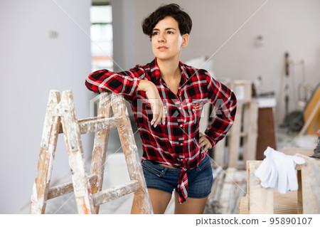 Pretty cottage owner in a plaid shirt and shorts posing in room being renovated Pretty cottage owner in a plaid shirt and shorts posing in room being renovated 95890107