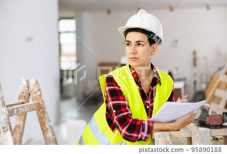 Focused young female civil engineer making notes at construction site indoors Focused young female civil engineer making notes at construction site indoors 95890188