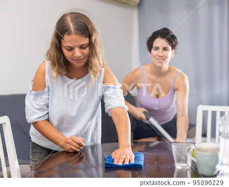 Young female couple cleaning living room together Young female couple cleaning living room together 95890229