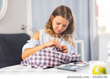 Young woman sewing on button at home 95890246