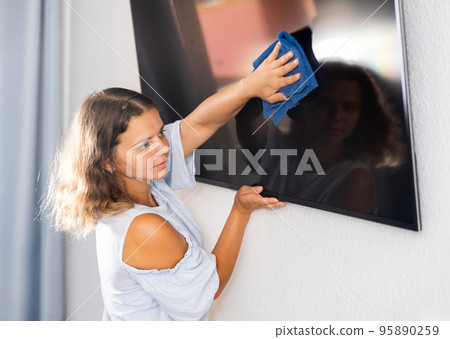 Young woman cleaning TV screen at home 95890259