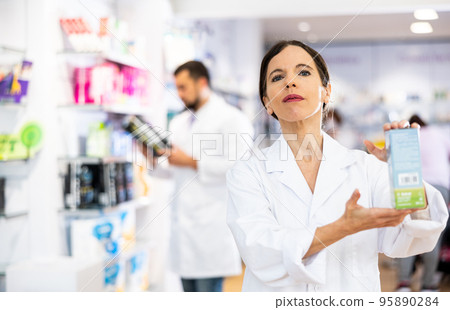 Female pharmacist offering product, working in drugstore Female pharmacist offering product, working in drugstore 95890284