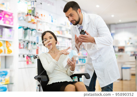 Pharmacist assisting woman in wheelchair in drugstore 95890352