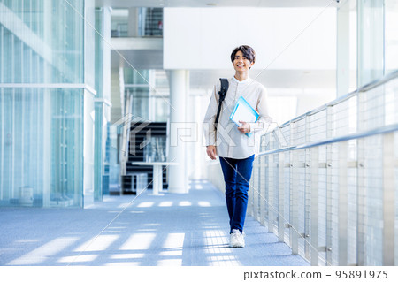 年輕男大學生站在校園走廊裡拿著筆記本 95891975