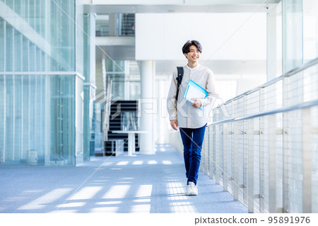 Young male college student standing with notebook in campus corridor 95891976