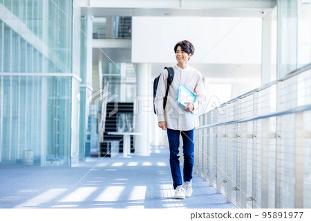 Young male college student standing with notebook in campus corridor 95891977