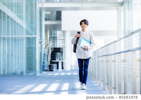 年輕男大學生站在校園走廊裡拿著筆記本 95891978