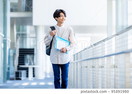 Young male college student standing with notebook in campus corridor Young male college student standing with notebook in campus corridor 95891980