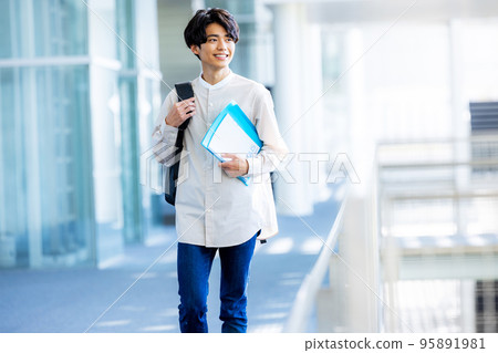 Young male college student standing with notebook in campus corridor 95891981
