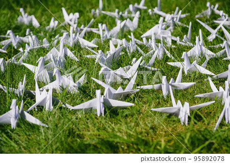 Japanese folded Origami cranes on fresh grass. Hundreds handmade paper birds on green field with copy space. 1000 thousand crane tsuru sculpture topic. Symbol of peace, faith, health, wishes and hope  95892078