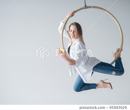 Caucasian female gymnast doing aerial hoop exercises and using smartphone.  95893026