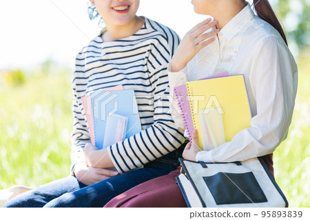 Two young female university students resting on a bench outdoors Two young female university students resting on a bench outdoors 95893839
