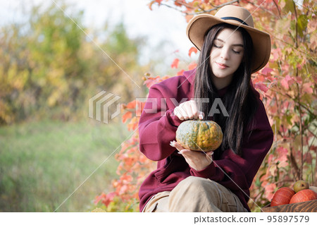 Happy young girl with pumpkin in autumn garden Happy young girl with pumpkin in autumn garden 95897579