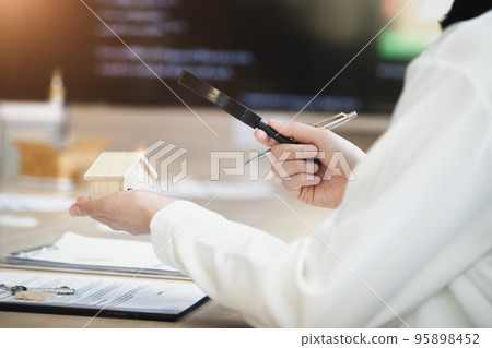Inspector Concept, a customer is holding a magnifying glass to look at each house model to check the price of a home loan for each model 95898452