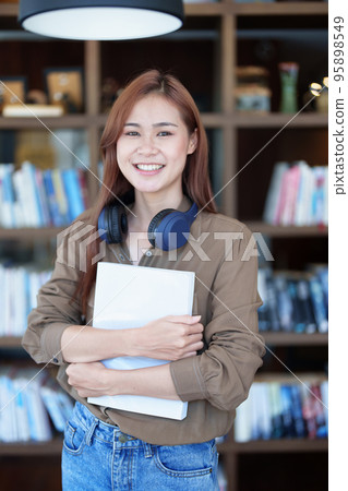 A portrait of a young Asian woman with a smiling face looking for a textbook in the library. A portrait of a young Asian woman with a smiling face looking for a textbook in the library. 95898549