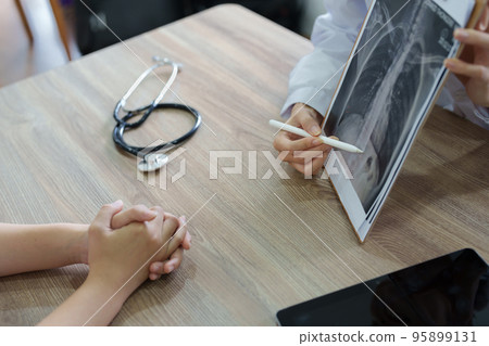 An Asian female doctor points to a patient x-ray film to explain the patient's treatment process. 95899131