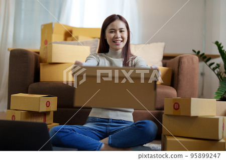 Portrait of a small startup Asian female entrepreneur SME owner picking up product before packing it in an inner box with a customer. Online Business Ideas and Freelance. 95899247