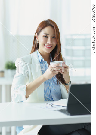 Portrait of an Asian businesswoman or business owner taking a coffee break while working in the office. Portrait of an Asian businesswoman or business owner taking a coffee break while working in the office. 95899766