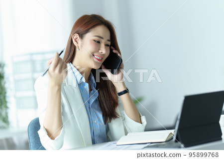 Portrait of an Asian businesswoman or business owner smiling and talking on a mobile phone in the office. 95899768