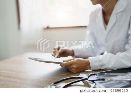 An Asian female doctor is using a tablet computer to analyze patient symptoms before treatment. An Asian female doctor is using a tablet computer to analyze patient symptoms before treatment. 95899920