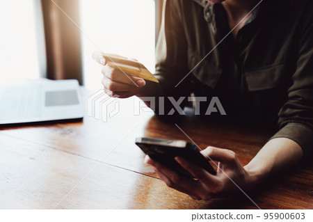 Portrait of young Asian woman using credit card and phone for online shopping. 95900603