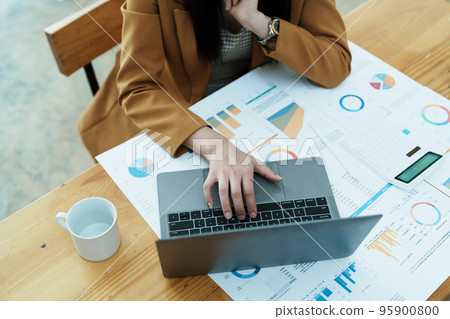 Portrait of a thoughtful Asian businesswoman looking at financial statements and making marketing plans using a computer on her desk. 95900800