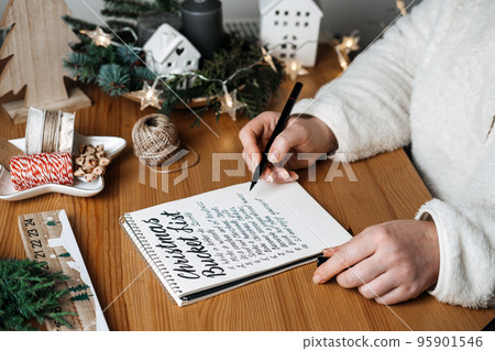 Christmas bucket list, countdown to Xmas checklist. Tasks you need to do in preparation for winter holidays. Woman writes in a notebook Christmas bucket list on table with gifts Christmas bucket list, countdown to Xmas checklist. Tasks you need to do in preparation for winter holidays. Woman writes in a notebook Christmas bucket list on table with gifts 95901546