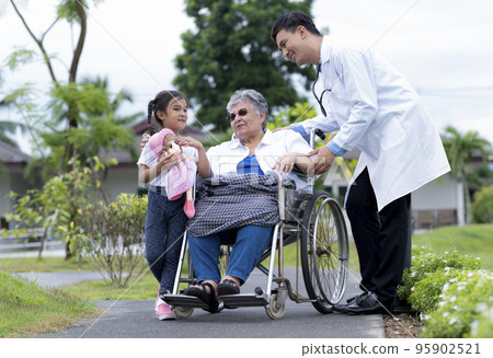 A young asian doctor and a young girl take care of an elderly middle eastern woman in a wheelchair. 95902521