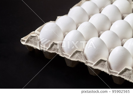 Cardboard tray with white chicken eggs on a dark background Cardboard tray with white chicken eggs on a dark background 95902565