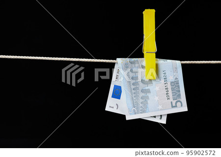 Five euro banknote fastened with a clothespin is dried on a clothesline on dark background Five euro banknote fastened with a clothespin is dried on a clothesline on dark background 95902572
