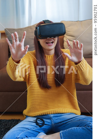 portrait of a young Asian woman using virtual reality simulator headset at home. portrait of a young Asian woman using virtual reality simulator headset at home. 95902701