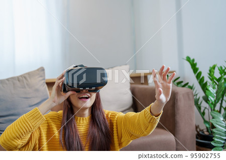 portrait of a young Asian woman using virtual reality simulator headset at home. portrait of a young Asian woman using virtual reality simulator headset at home. 95902755