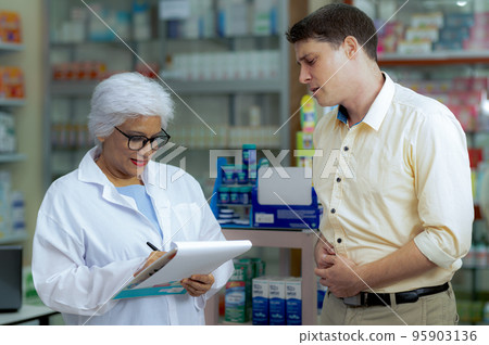 A young man consults a pharmacist to buy medicine for stomach pain. 95903136