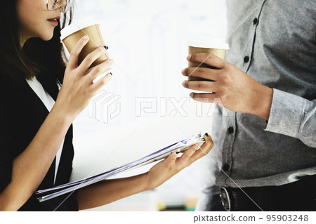 Focus on a woman's hand holding a cup of coffee and chatting with a coworker during the afternoon break 95903248