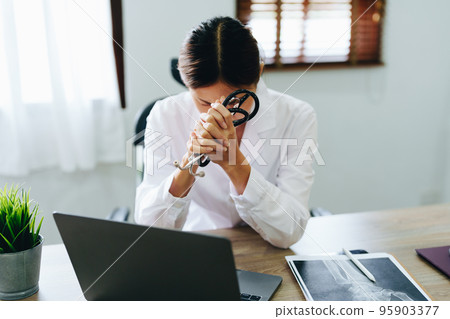 An Asian female doctor uses a computer while showing concern about patient information. An Asian female doctor uses a computer while showing concern about patient information. 95903377