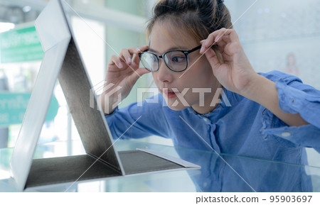The girl tried on the glasses and looked in the mirror. The girl tried on the glasses and looked in the mirror. 95903697