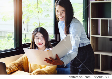 Two female company employees happily smiled at each other as they handed each other folders 95903977
