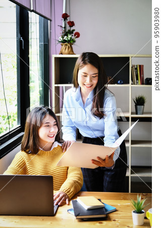 Two female company employees happily smiled at each other as they handed each other folders 95903980