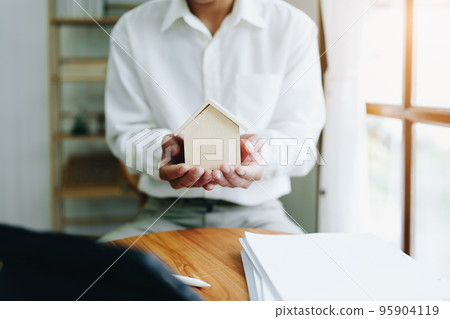 Accountant, businessman, real estate agent, Asian business man handing model house to customers along with house interest calculation documents for customers to sign. 95904119