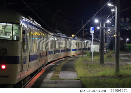 Local train and conductor leaving local station at night 95904971
