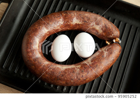 Homemade kangal sucuk made from spice mixtures used and two white egg in Turkish cuisine in a heavy black cast iron grill pan 95905252