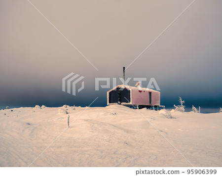 Minimalistic background with of lonely red cabin in winter under dramatic sky. Dubladom on the mountain Volodyanaya Kandalaksha, Murmansk region in Russia. 95906399