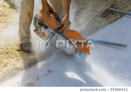 Construction worker uses diamond blade saw to cut concrete sidewalk 95906431