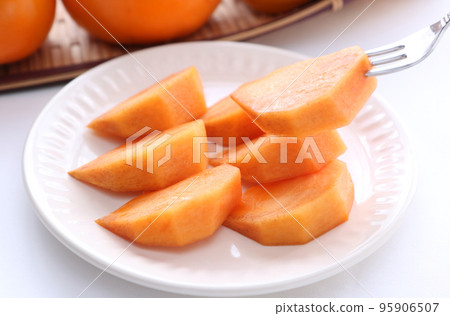 7 slices of cut persimmons on a white circular plate with a white background and 3 round persimmons on the top (bottom focus) 7 slices of cut persimmons on a white circular plate with a white background and 3 round persimmons on the top (bottom focus) 95906507