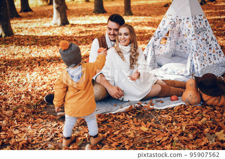 Family have fun in a autumn park. Cute blode in a white sweater. Parents with little son. Family sitting near wigwam. Family have fun in a autumn park. Cute blode in a white sweater. Parents with little son. Family sitting near wigwam. 95907562