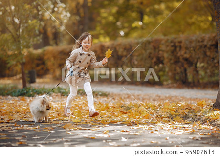 Cute child in a autumn park. Elegant little lady with a dog. Girl in a brown coat. Cute child in a autumn park. Elegant little lady with a dog. Girl in a brown coat. 95907613