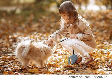 Cute child in a autumn park. Elegant little lady with a dog. Girl in a brown coat. 95907639