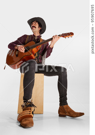 Portrait of man with moustaches in vintage style clothes playing guitar, performing isolated over white background. Country music 95907695