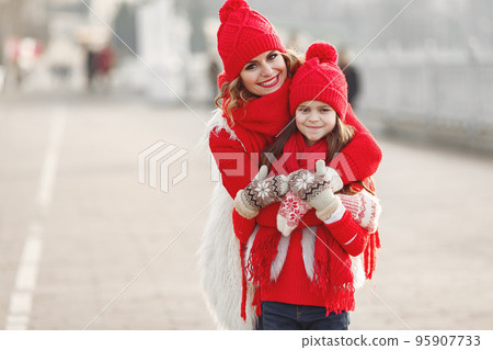 Mother and child in knitted winter hats on family Christmas vacation. Handmade wool hat and scarf for mom and kid. Knitting for kids. Knit outerwear. Woman and little girl in a park. 95907733